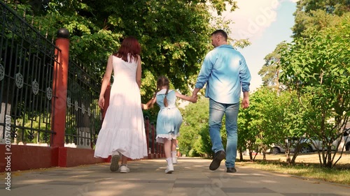 Kid girl, parents walking in city park. Mother father walking hand in hand on street. Child daughter, playing with parents outdoors. Happy family. Family weekend, summer park. Mom dad, daughter child