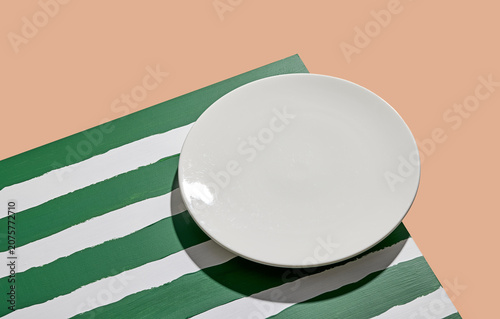 Minimalist food mockup with empty ceramic plate on striped green background. Flat lay concept for menu or recipe