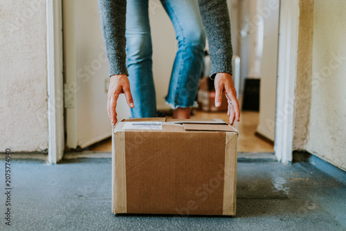 Photos Person picking up a cardboard package from the doorstep, wearing jeans and a sweater