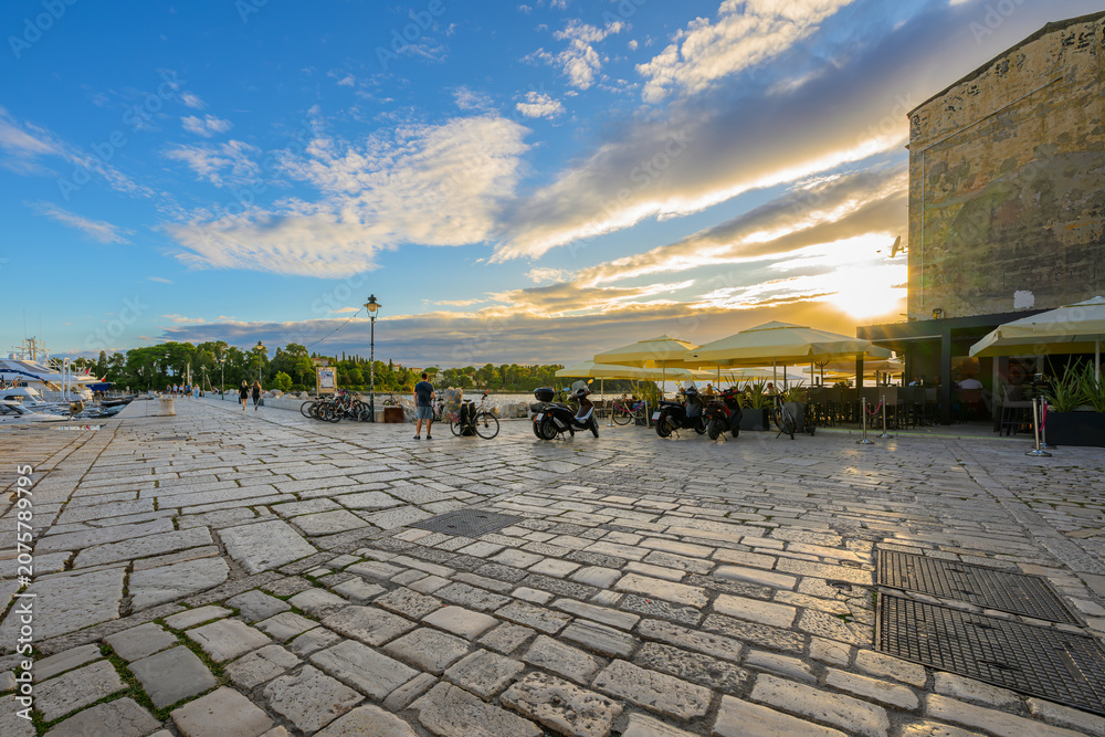 Fototapeta premium Sunset sky above sidewalk cafes and marinas at the seaside promenade of Rovinj, Croatia, on the Istrian Peninsula of the Adriatic Sea.