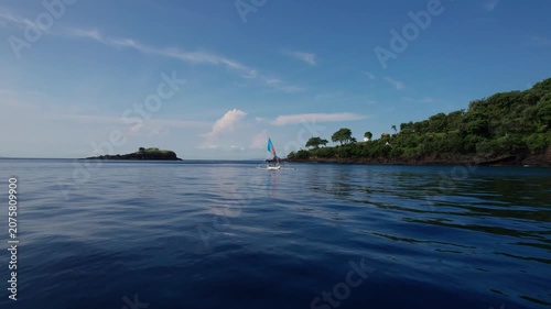 Aerial View of Traditional Outrigger Sailboat with Colorful Sail on Clear Tropical Ocean