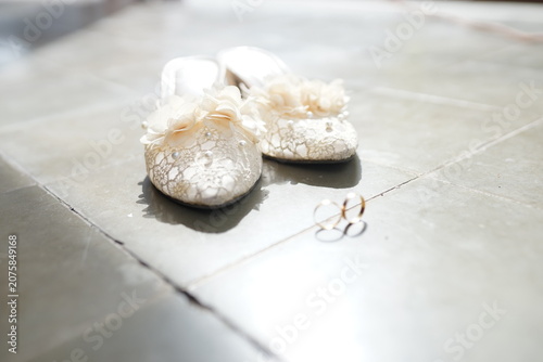 Elegant white lace bridal shoes and gold wedding rings on floor romantic ceremony morning light detail