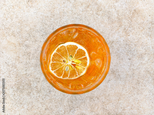 Iced lemon tea beverage in glass with slice of citrus and ice cubes on textured background. Refreshing cold drink top view overhead.