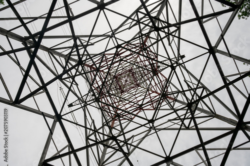 Принти на полотні Abstract symmetrical view looking up through the steel lattice framework of a high-voltage power transmission tower against a pale sky