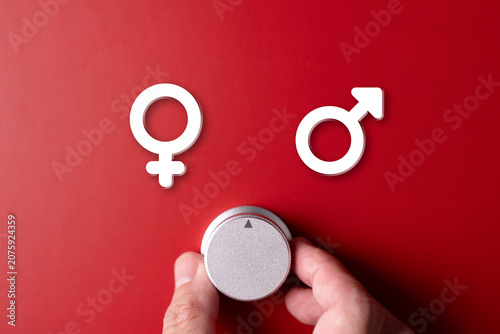 A hand adjusts a dial between male and female symbols on a red background, symbolizing a choice between genders.