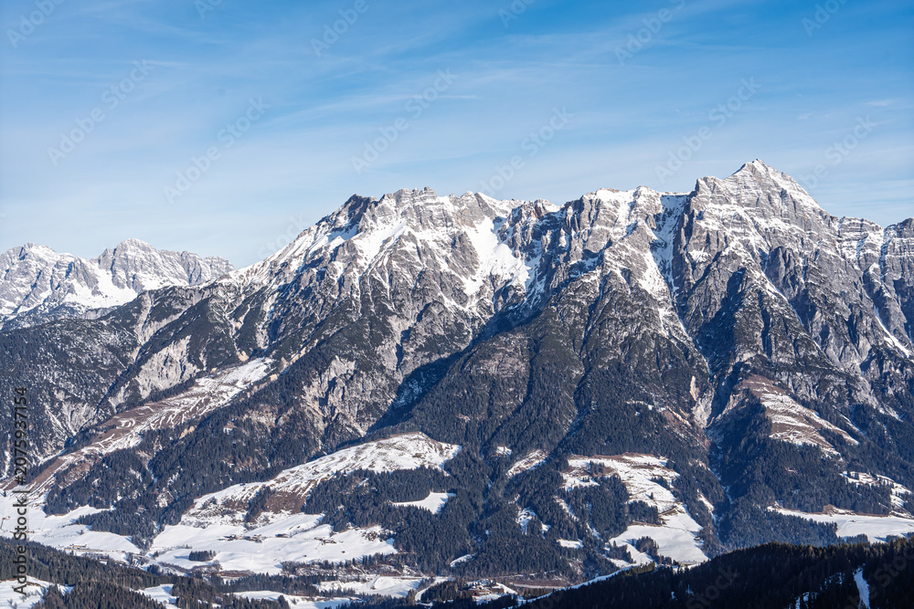 Obraz premium A breathtaking panoramic view of majestic snow-covered Alpine mountain peaks in Saalbach Hinterglemm, Austria, captured on a clear sunny day during the peak winter ski season.