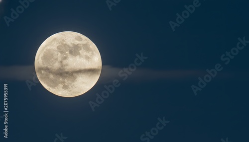 Glowing August full moon supermoon shining bright in the dark night sky with thin wispy clouds passing across it for astrology and celestial space exploration concept