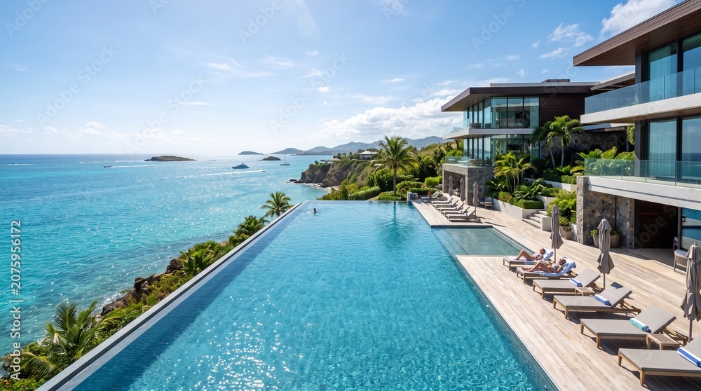 Fototapeta premium Stunning luxury infinity pool overlooking a turquoise tropical ocean at a modern Caribbean villa with sun loungers and expansive architectural design on a sunny day