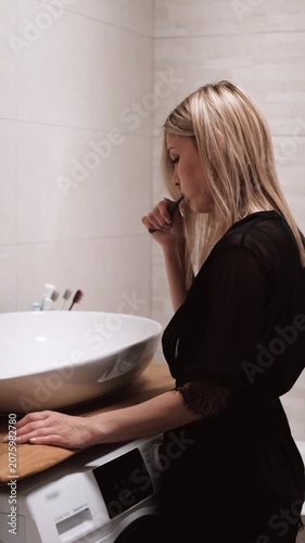 Morning routine: A beautiful blonde brushing her teeth in the bathroom. Side view.