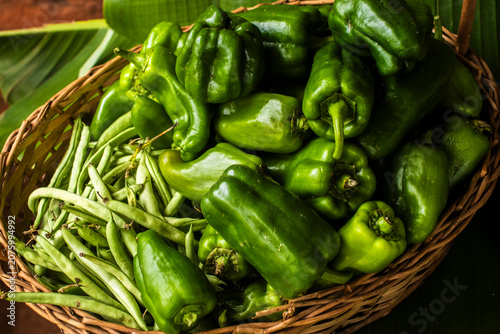 High-angle shot of a rustic wicker basket filled with fresh, organic green bell peppers and crisp green beans. 
