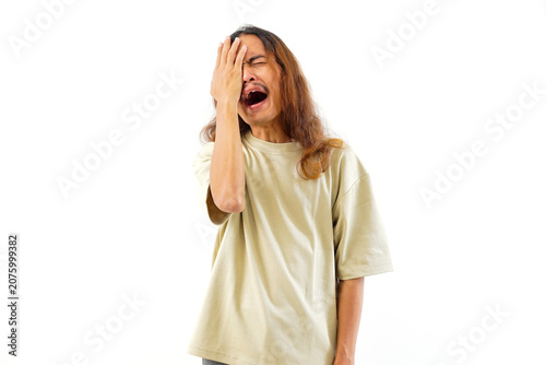 Photos A young Asian man with long hair expressing frustration or disappointment by covering his face with his hand, isolated on a clean white background