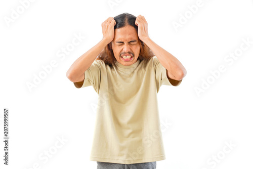 A young man with long hair wearing a beige t-shirt, clutching his head with both hands, showing an expression of intense stress, frustration, or a headache.