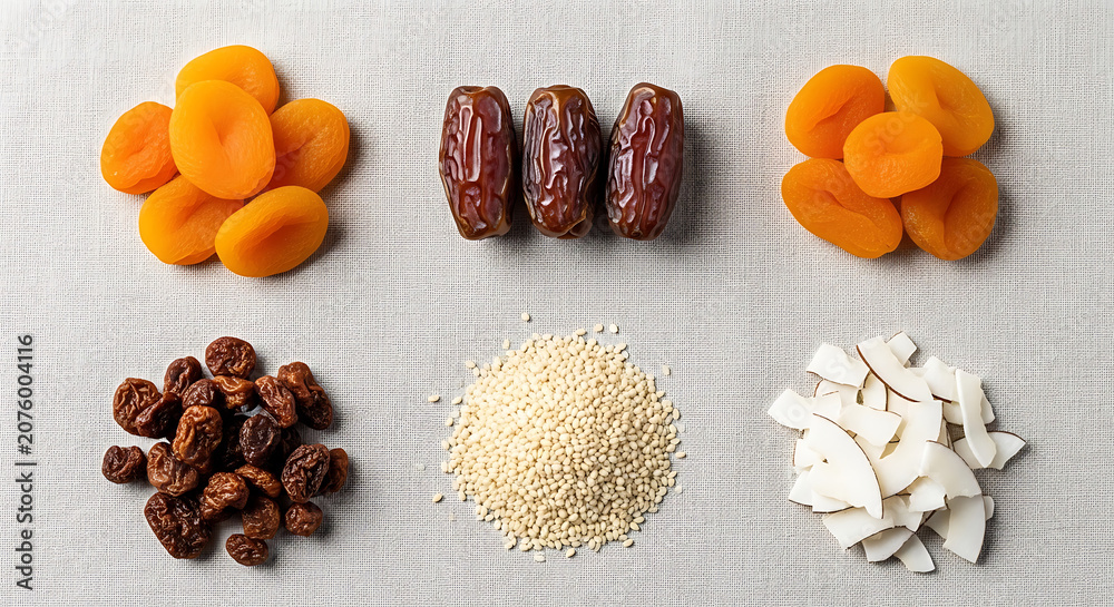 Fototapeta premium Dried apricots, dates, raisins, sesame seeds, and coconut flakes on gray fabric