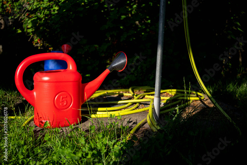 Vibrant red plastic water can and yellow garden  water hose near the water tap.
