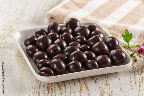 Принти на полотні Dark chocolate coated candies in white dish on rustic wooden table with striped