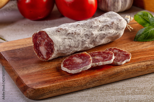 Obraz na plátne Sliced dry cured salami sausage on a wooden cutting board with fresh tomatoes, garlic, and basil