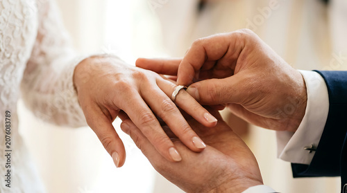 A heartfelt close-up captures the tender moment as a groom places a radiant wedding ring on his bride's finger, symbolizing enduring love and commitment during their beautiful marriage ceremony
