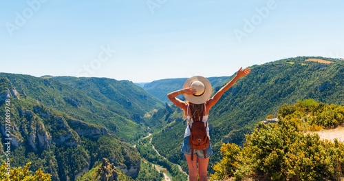 Happy and freedom female hiker with backpack looking at canyon landscape with raised arm