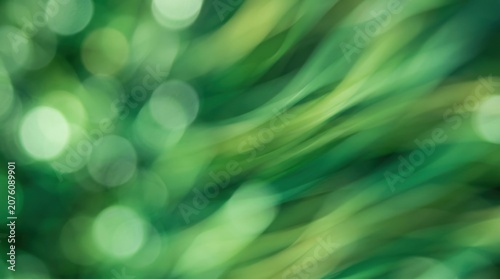A blurred, abstract image of lush green foliage. The photograph captures the movement of leaves and branches, creating a sense of depth and dynamism.