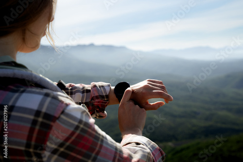 Fotografie A woman is using a smartwatch while on a hiking trip, with blurred mountain scenery in the background