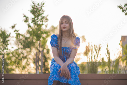 Gentle young woman in blue floral dress smiling in golden hour sunset with copy space