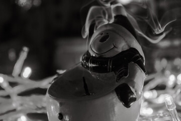 Black and white close up portrait of a ceramic snowman figurine with smoke