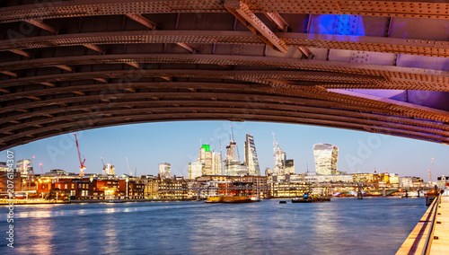 City of London skyline over River Thames

Description:
City of London skyline over the River Thames at dusk, framed by a bridge with modern skyscrapers, construction cranes and illuminated financial d