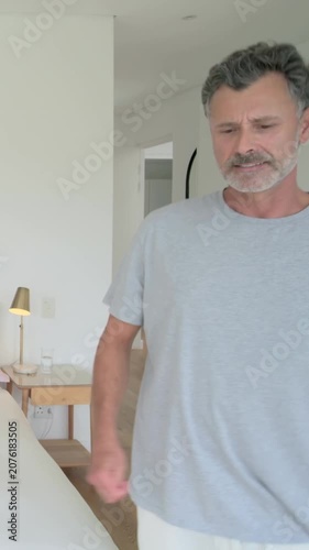 Vertical video: Adjusting mattress in bedroom, man gray tee white shorts spreading duvet making bed