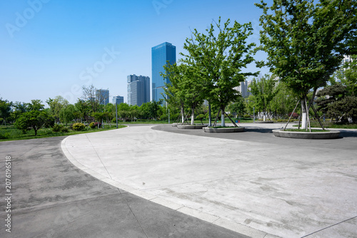 Rizhao city park with green trees concrete plaza and distant modern skyscrapers under clear blue sky