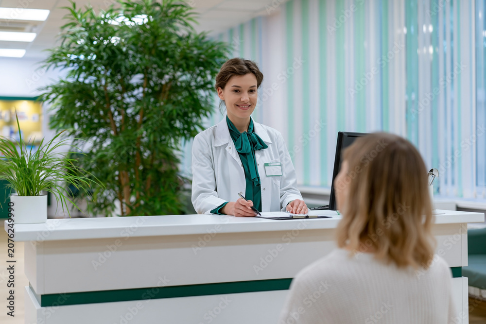 Obraz premium Smiling medical receptionist assisting patient at hospital reception desk in modern clinic