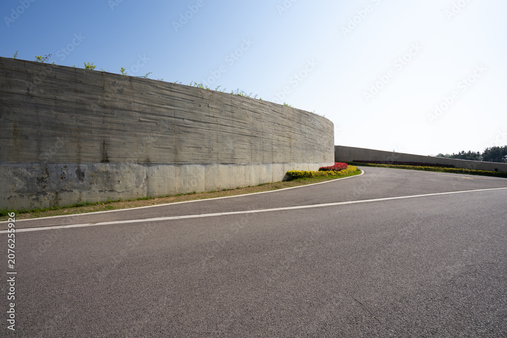 Obraz premium Curved asphalt road beside concrete retaining wall under bright sunlight