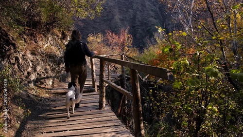 view of a female hiker with a dog walking on a wooden path in Turgen Gorge, Kazakhstan. Commercial background for travel, active lifestyle, eco-tourism, and mountain adventure concepts.