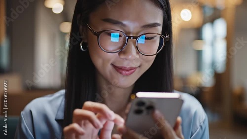Young woman with glasses using smartphone in cafe.