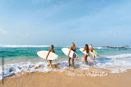 Photography Four women with surfboards walk into sea waves on sunny beach