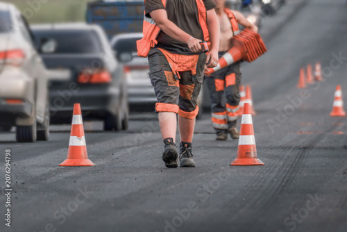 Road workers placing traffic cones during road repair on a busy city street, lane closure, asphalt resurfacing and traffic control