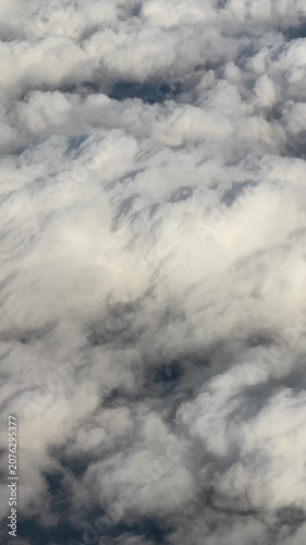 Aerial view of stratocumulus cloud canopy drifting across sky, slowly thinning and breaking to reveal dark land patches near frame edge, soft light, layered texture, calm drift now