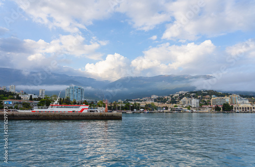 Schilderij op canvas View of the Yalta embankment from the sea, mountains in clouds and a pier with a