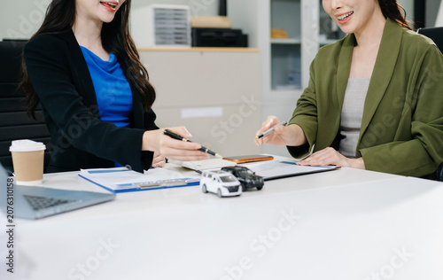 Asian businesswoman signs a car loan contract, receives the vehicle key, and shakes hands with a finance agent. Ideal for commercial auto insurance