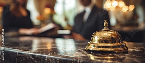 A brass service bell sits on a marble counter in front of blurred staff
