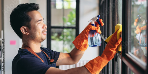 Foto Housekeeper man in orange rubber gloves using a clean spray and