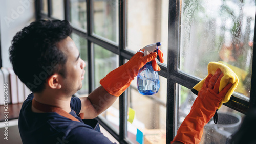 Bild auf Leinwand Housekeeper man in orange rubber gloves using a clean spray and