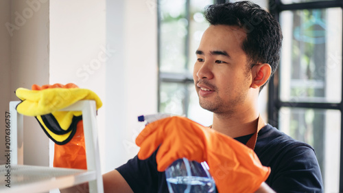 Cuadro en lienzo Housekeeper man in orange rubber gloves using a clean spray and