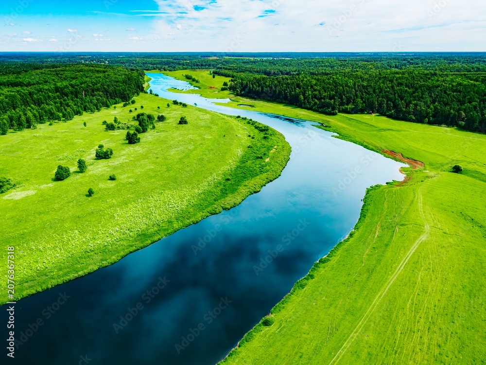 Obraz premium Curving river cutting through lush green fields and dense forest under a clear blue sky