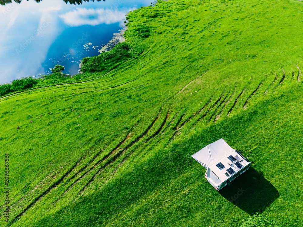 Obraz premium Camper van parked on lush green grass near tranquil water reflecting blue sky