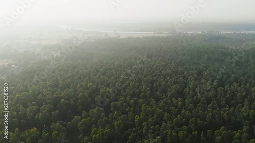 Aerial view of vast terai forest expanse near Jhapa at dawn or dusk; hazy atmosphere with a large water body visible on the horizon