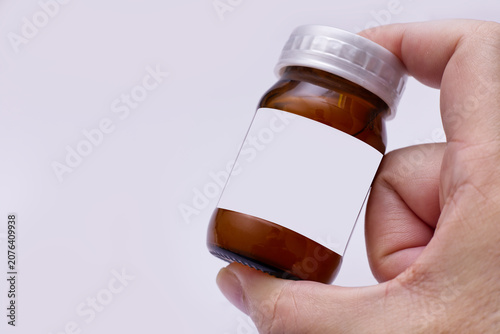 Hand holding amber glass medicine bottle with a blank white label, isolated on white background. Perfect for mockup product design or pharmaceutical branding