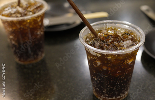 Close-up of a refreshing iced cola soft drink with fizzy bubbles in a clear plastic cup and a brown straw, served on a restaurant table