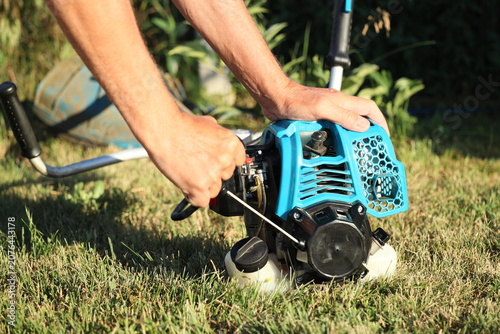 Close-up of a man starting a gas grass trimmer engine on the lawn
