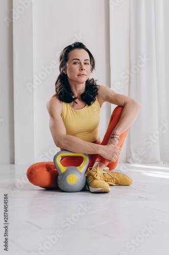 Fotografie Fit woman resting on floor beside kettlebell in bright fitness studio after trai