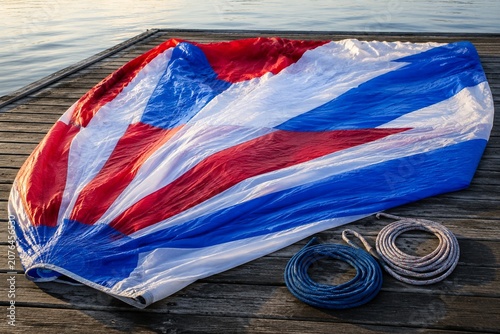 Red white and blue spinnaker sail laid flat on dock with coiled ropes, morning light.